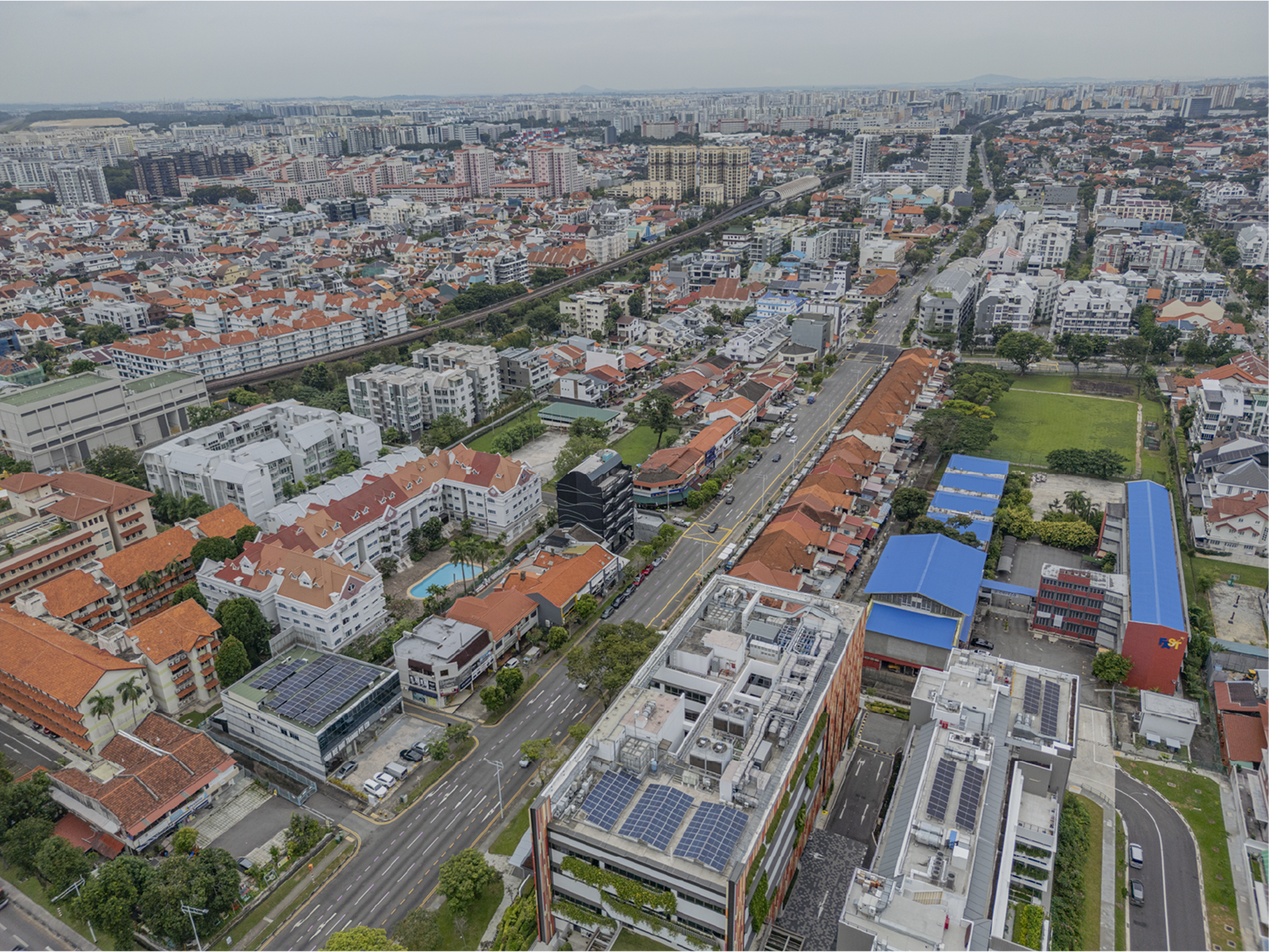 Aerial view of a dense city with various buildings, roads, and greenery under a cloudy sky.